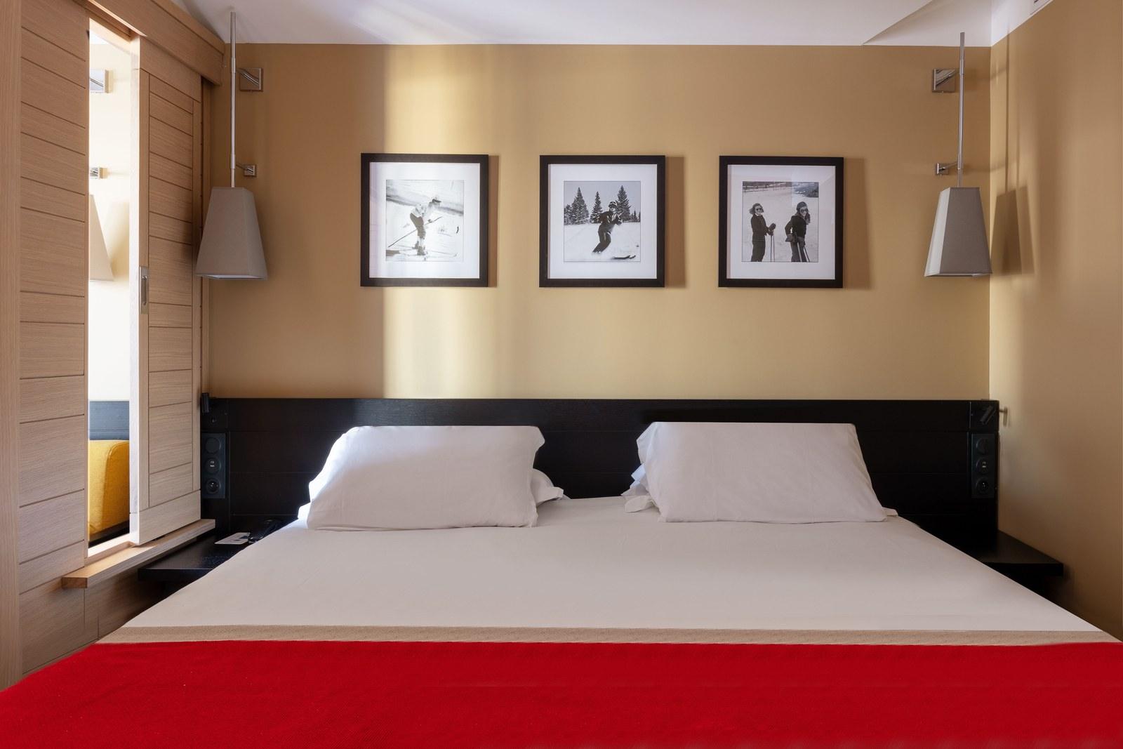 Bedroom with white bedding, a red runner and timber details at Club Med Peisey-Vallandry