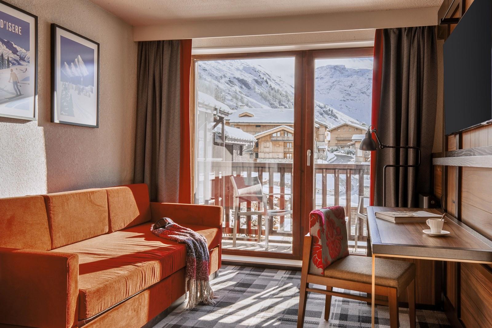 Living area with an orange sofa and a snowy balcony view at Club Med Val d’Isère
