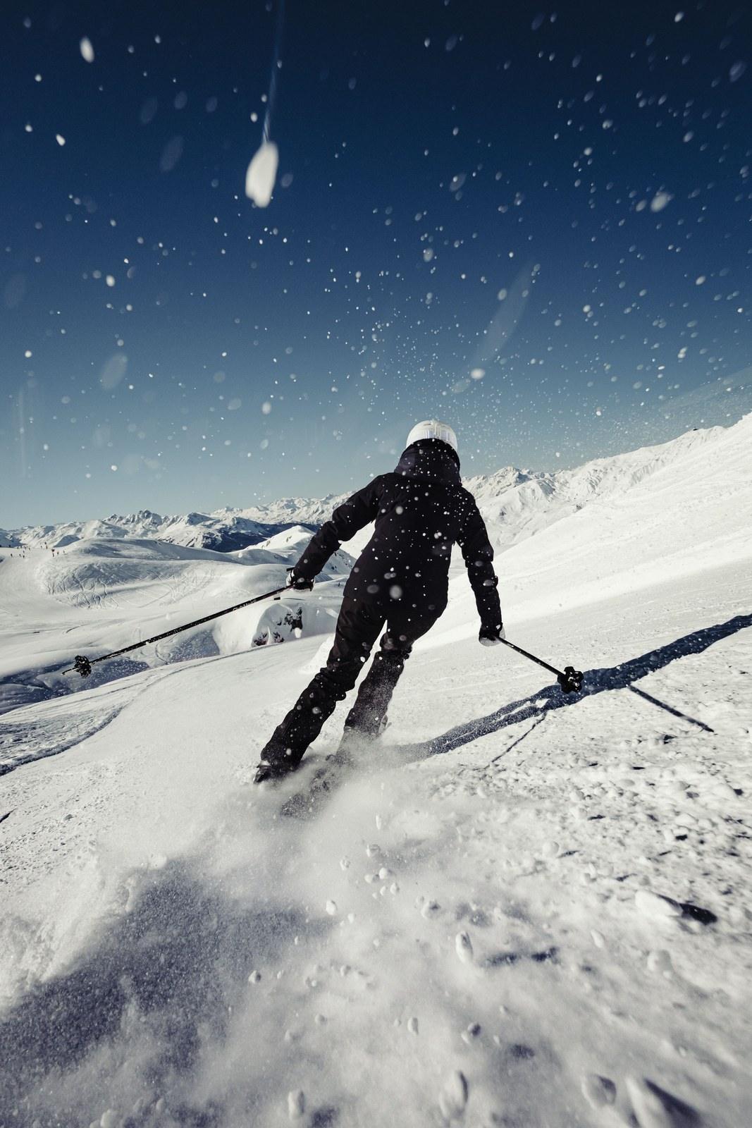 Skier carving through snow above mountain slopes at La Plagne