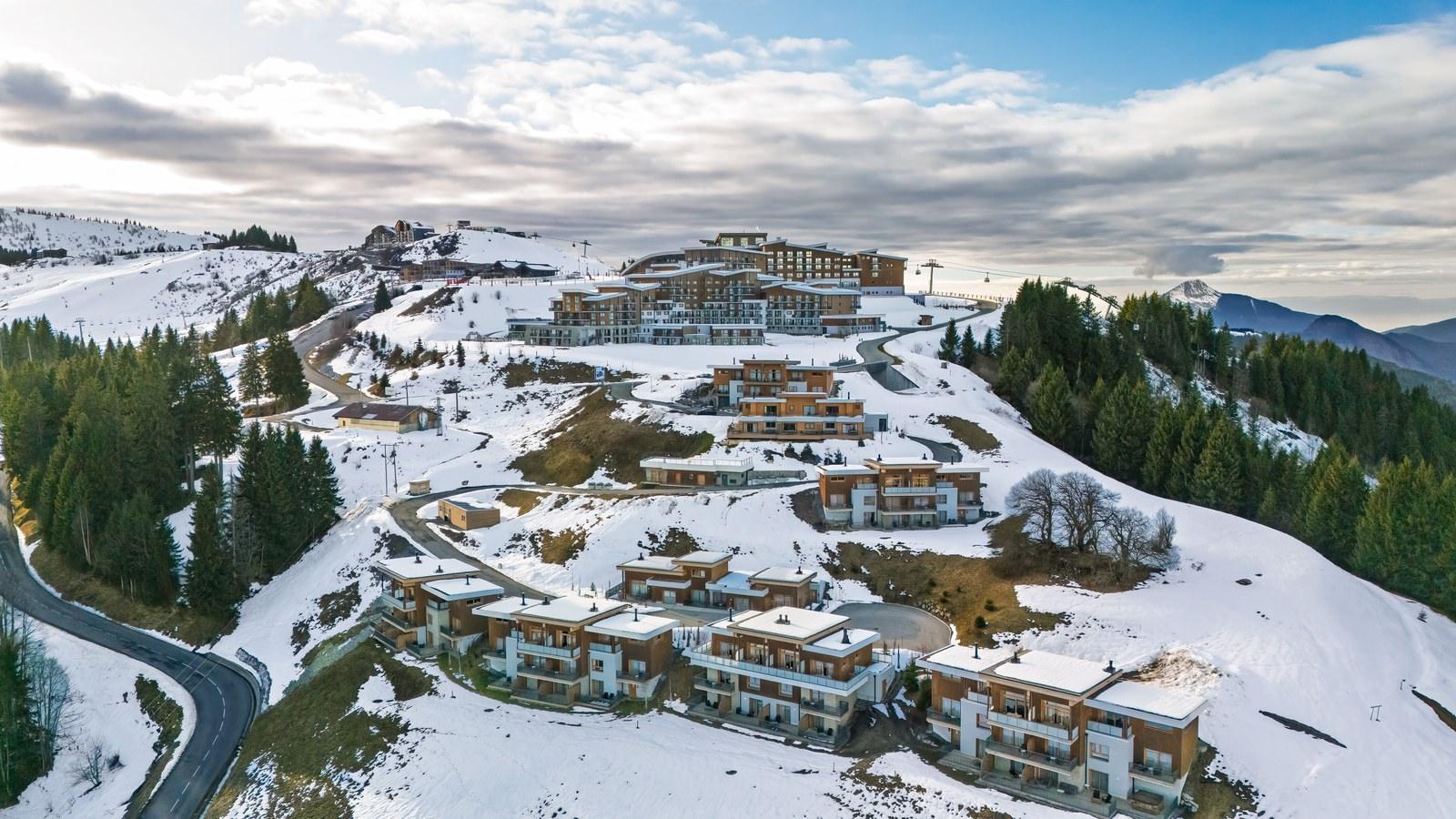 Aerial view of Grand Massif Chalet-Apartments with patchy snow and the main resort uphill