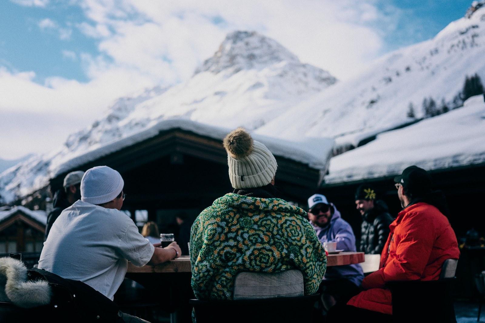 Adults sharing hot drinks on a terrace at Club Med Val d’Isère with snowy mountains behind