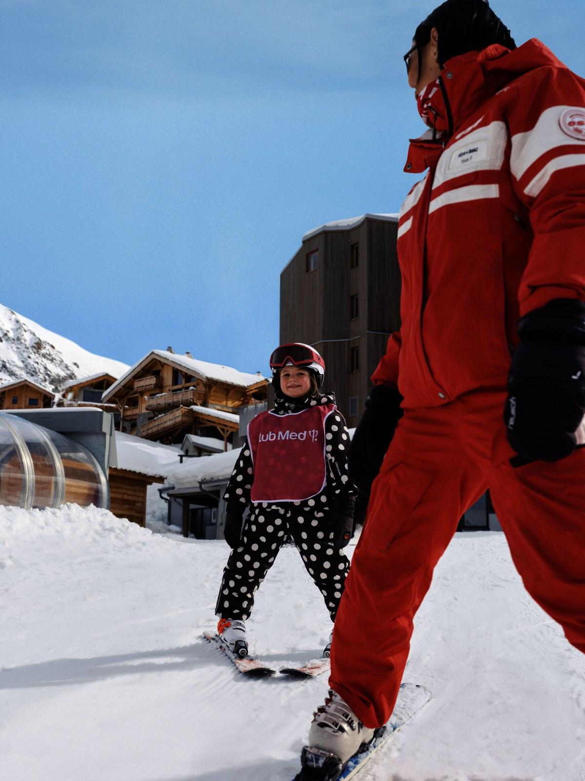 Child learning to ski beside an instructor at Club Med Alpe d’Huez