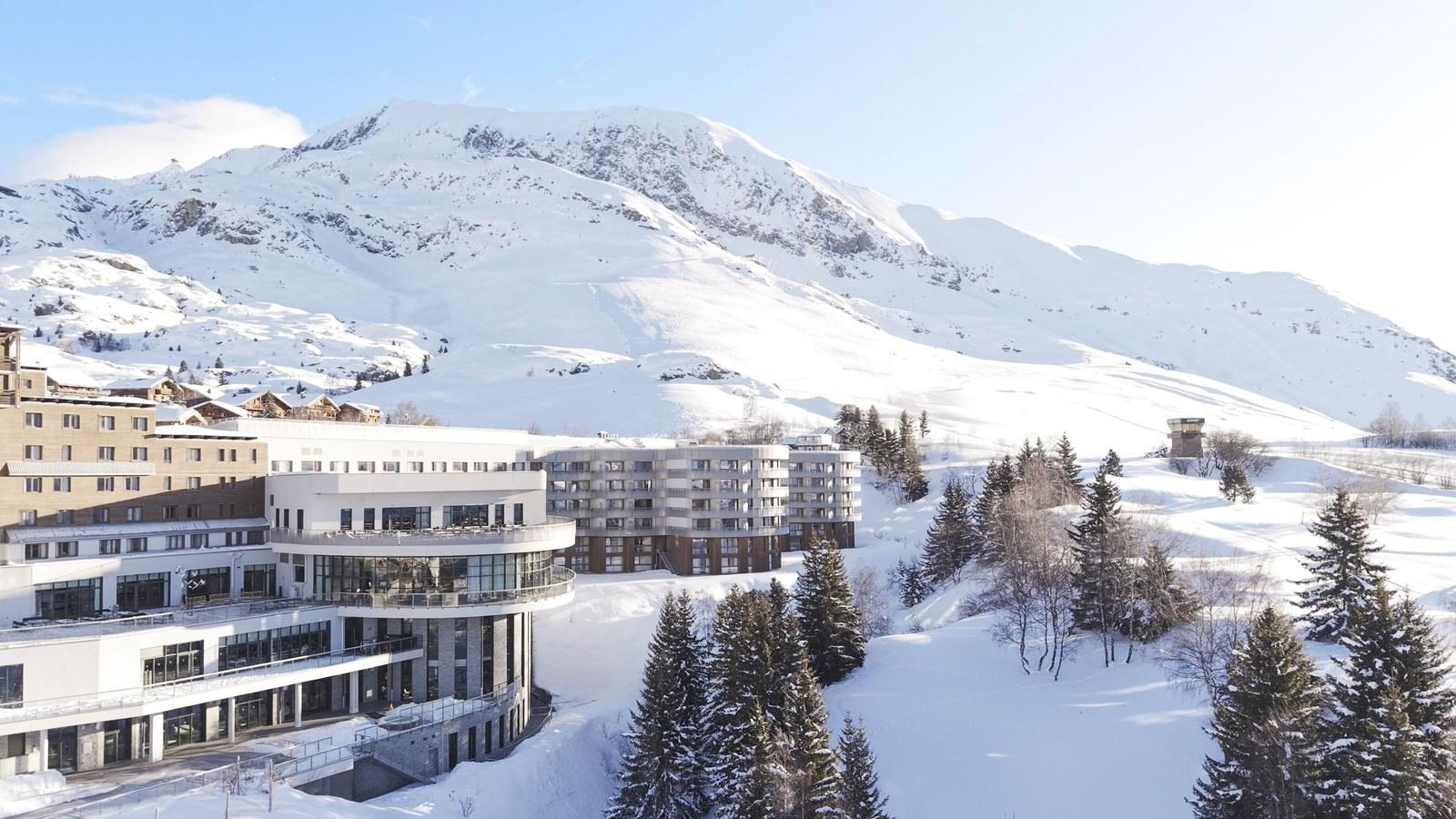 Snow-covered Club Med Alpe d’Huez beneath a mountain ridge