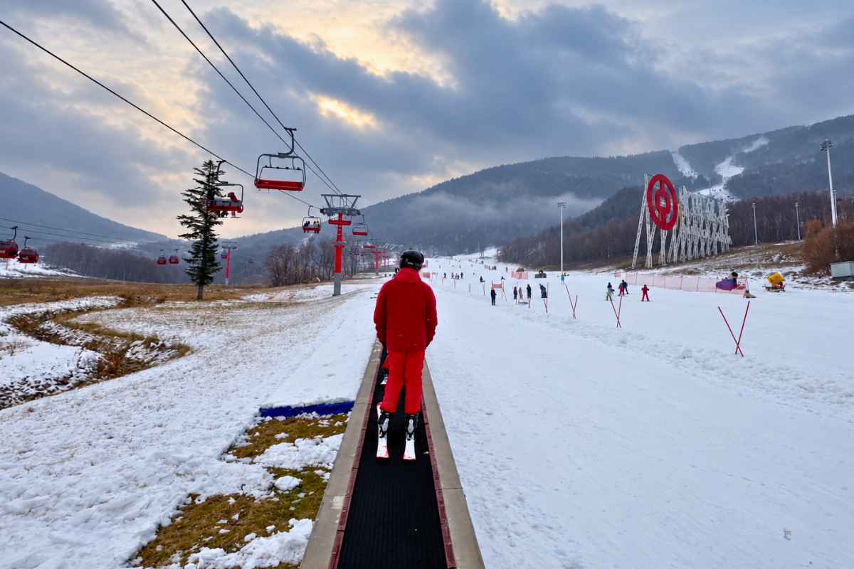 Skier on a conveyor lift beside the slopes and chairlifts at Beidahu